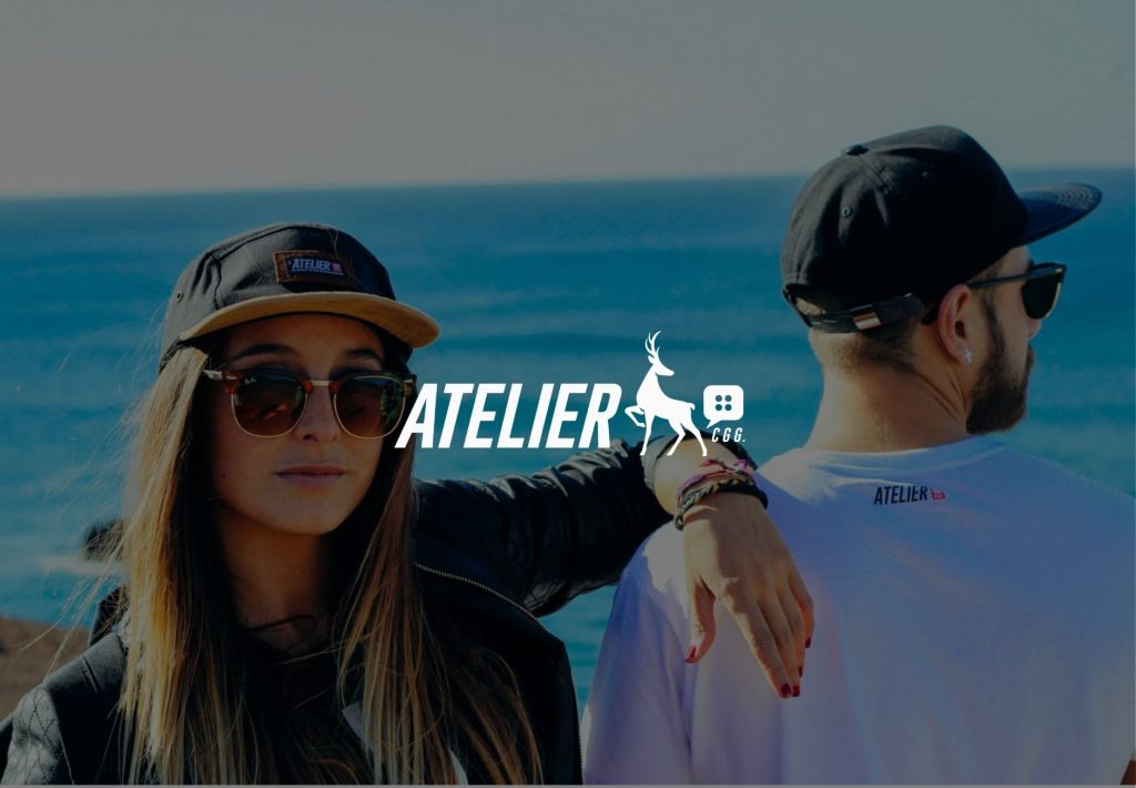 Dos modelos con gorras y gafas de sol luciendo ropa de la marca Atelier CGG frente al mar