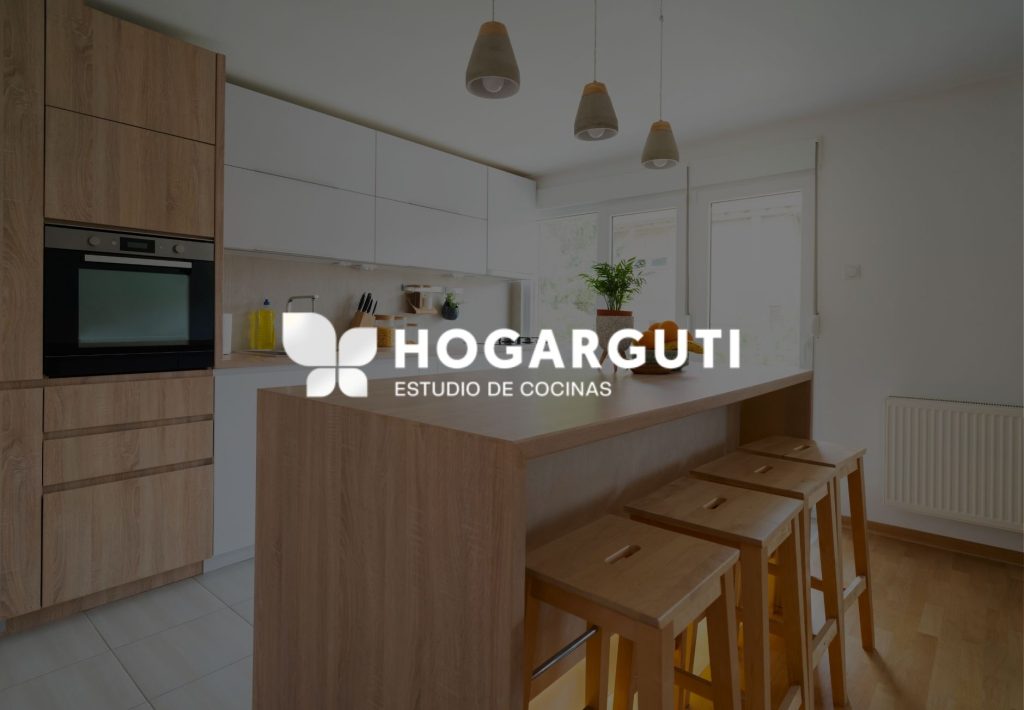 Cocina moderna con isla de madera, taburetes y muebles blancos. Estudio de cocinas Hogarguti.