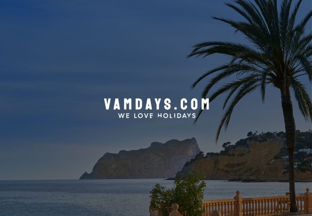 Vista mediterránea con palmera, acantilados y mar en calma al atardecer con logo Vamdays.com agencia de viajes