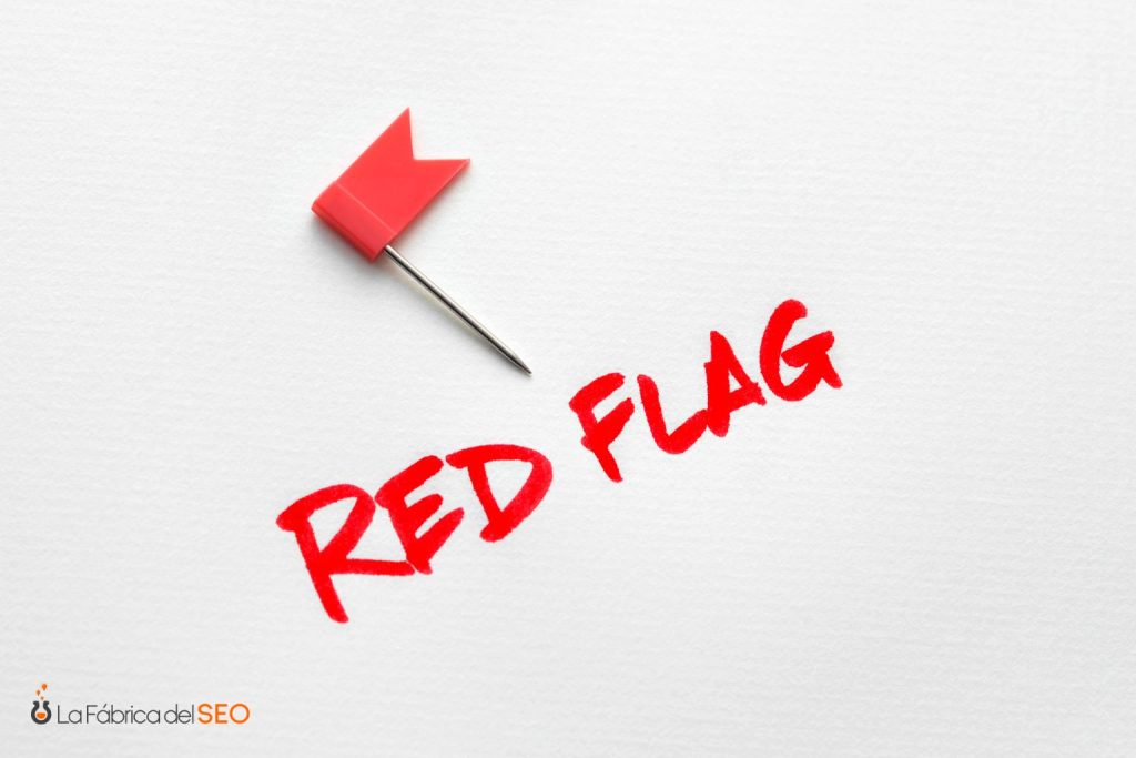 Chincheta roja con bandera junto al texto "Red Flag" escrito en rojo, señal de alerta en SEO y GEO