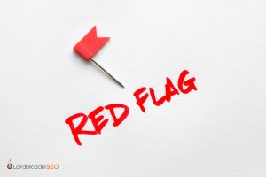 Chincheta roja con bandera junto al texto "Red Flag" escrito en rojo, señal de alerta en SEO y GEO