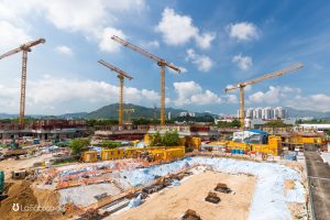 Gran obra de construcción con cinco grúas torre amarillas, módulos prefabricados y maquinaria pesada en sitio urbano