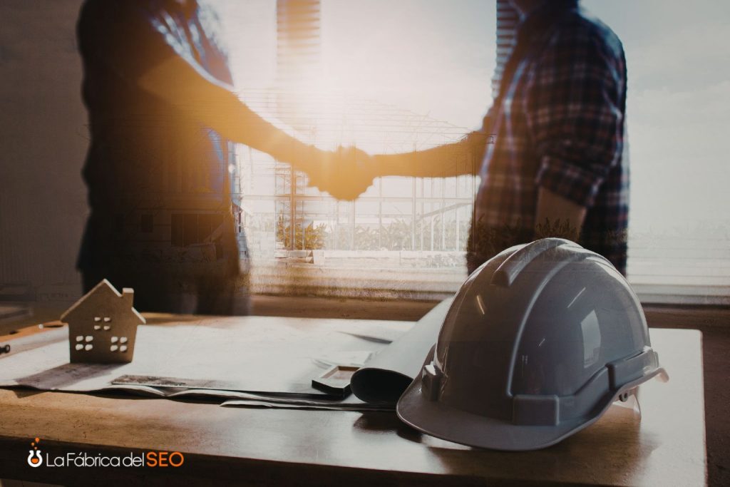 Apretón de manos entre profesionales de construcción con casco de seguridad y maqueta de casa sobre mesa de trabajo