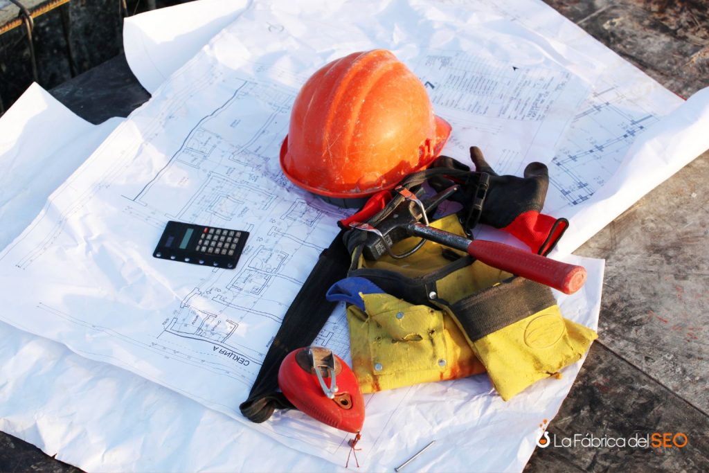 Casco de seguridad naranja, cinturón de herramientas y calculadora sobre planos de construcción en obra