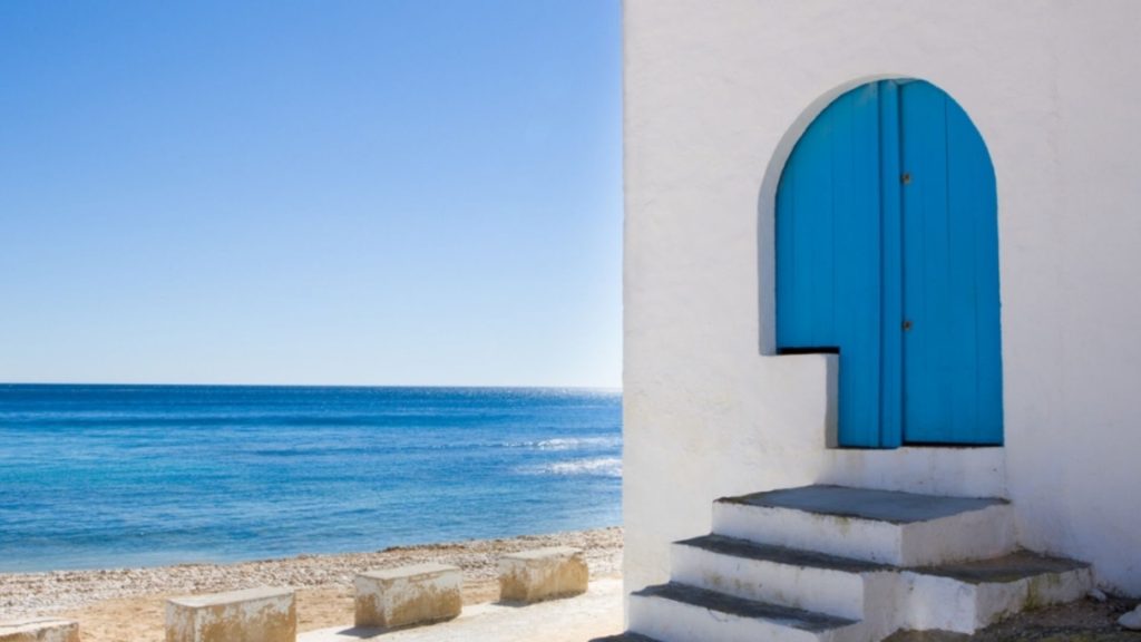 Puerta arqueada azul en edificio blanco mediterráneo junto a la playa de Cala Portixol con mar turquesa