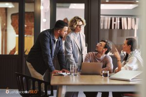 Equipo de agencia SEO reunido analizando estrategia digital con laptop en sala de trabajo moderna