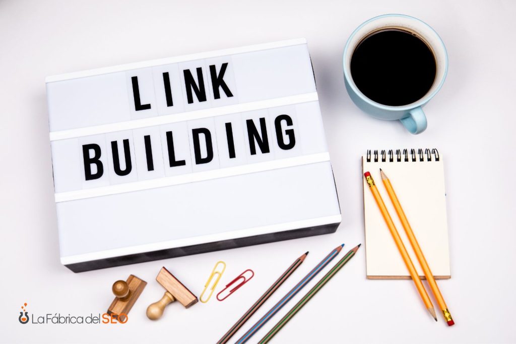 Letrero luminoso con el texto Link Building rodeado de lápices, libretas, sellos y café, concepto SEO
