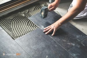 Instalación de cerámica gris en suelo con mortero y mazo de goma por albañil profesional
