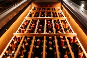 Bodega de enoturismo con botellas de vino tinto almacenadas en rack de madera con iluminación cálida
