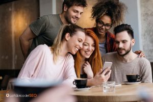 Grupo de amigos jóvenes disfrutando en restaurante mientras comparten contenido en smartphone tomando café