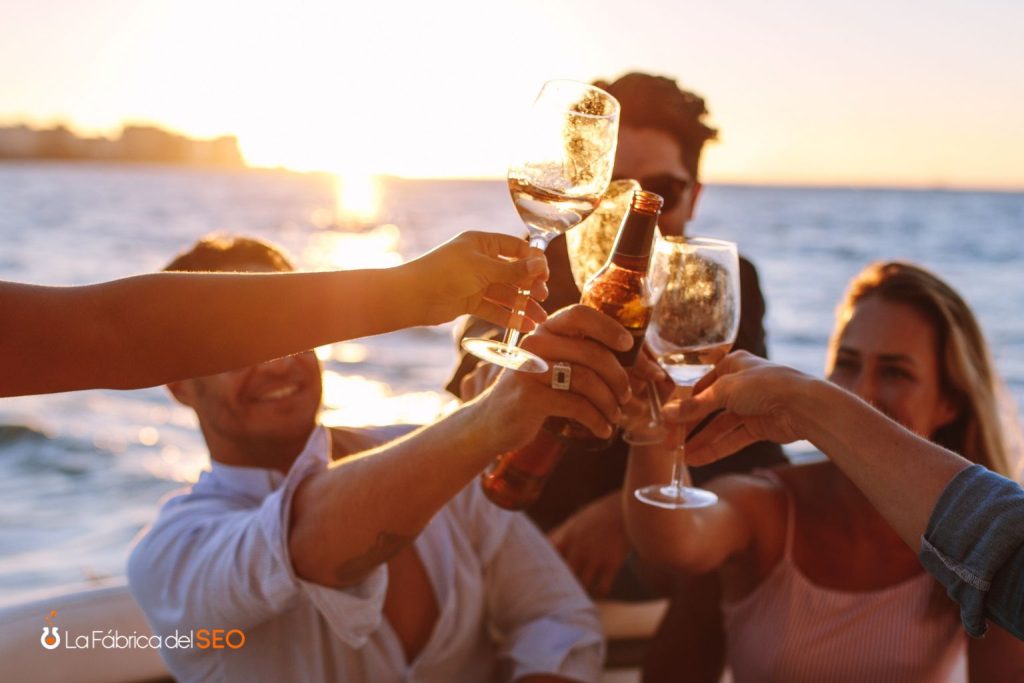 Grupo de amigos brindando con copas de vino y cerveza al atardecer en el mar desde un barco