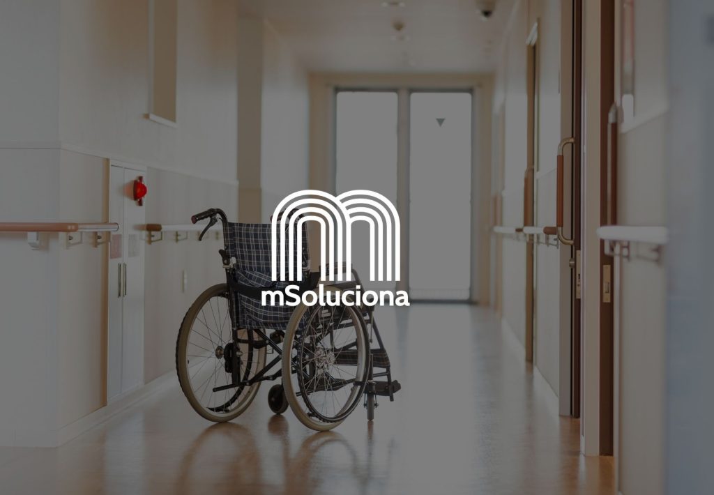 Silla de ruedas vacía en pasillo de centro de salud con logo de mSoluciona, empresa de soluciones sociosanitarias