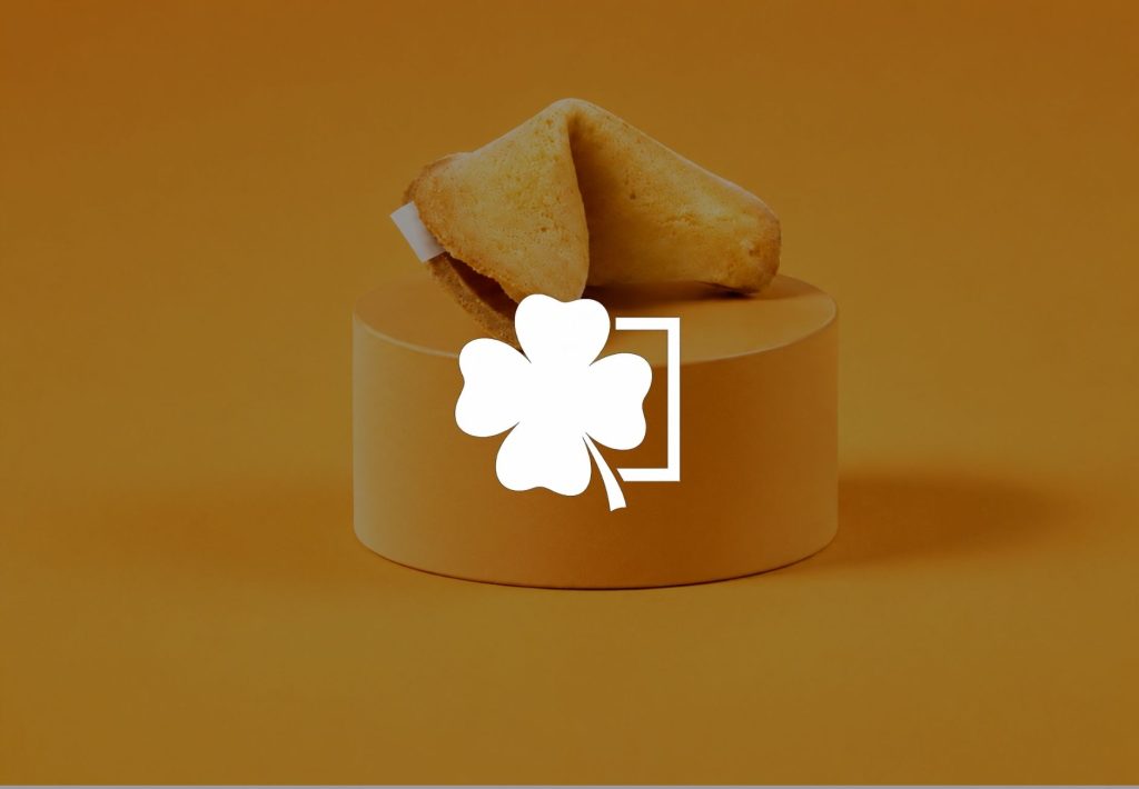 Galleta de la fortuna abierta sobre pedestal dorado con trébol de cuatro hojas blanco, símbolo de buena suerte