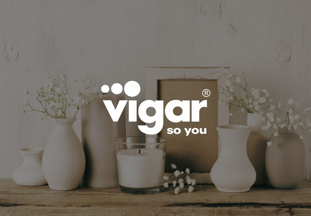 Logo de Vigar So You sobre fondo con jarrones cerámicos blancos, velas y flores silvestres en estilo minimalista