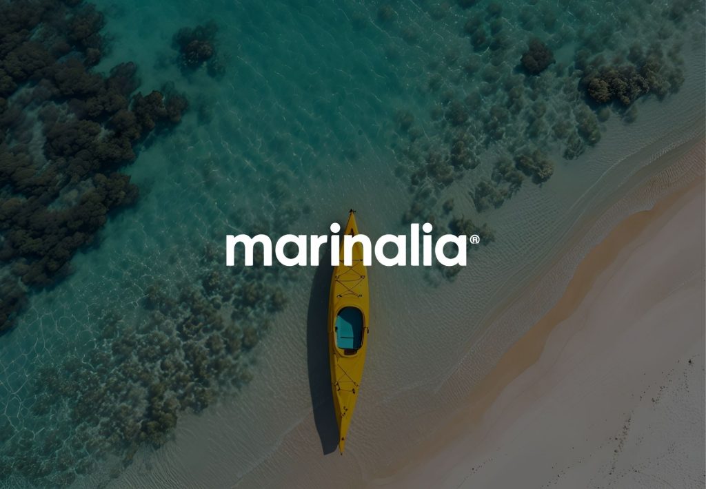 Kayak amarillo en aguas turquesas junto a arrecife de coral y playa de arena blanca, logo Marinalia