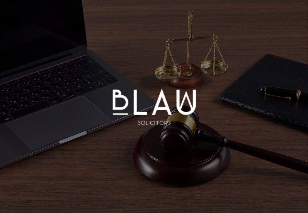 Logo de Blau Solicitors sobre escritorio con mazo judicial, balanza de justicia y portátil