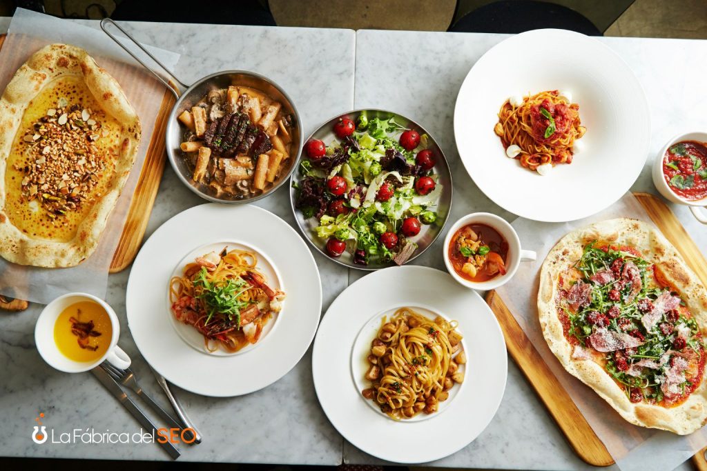 Carta de restaurante italiano con pizzas, pasta, ensalada y salsas servidos en mesa de mármol