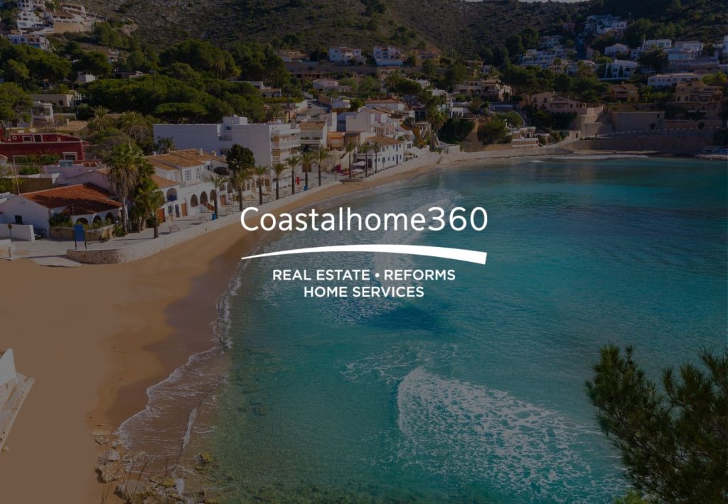 Vista aérea de cala mediterránea con playa de arena, aguas turquesas y villas blancas en la costa española de Coastalhome360