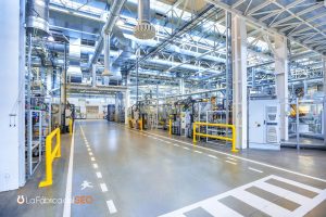 Interior de planta de fabricación industrial moderna con maquinaria automatizada, barreras de seguridad amarillas y señalizac
