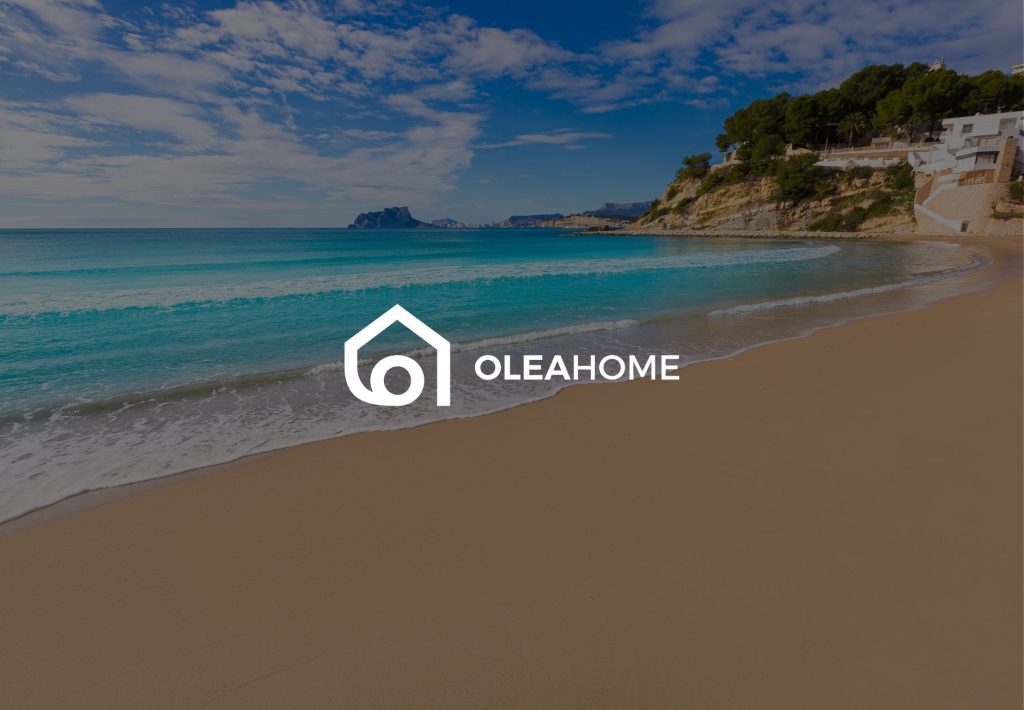 Logo de Oleahome sobre playa mediterránea con aguas turquesas, arena dorada y acantilados en la Costa Blanca española