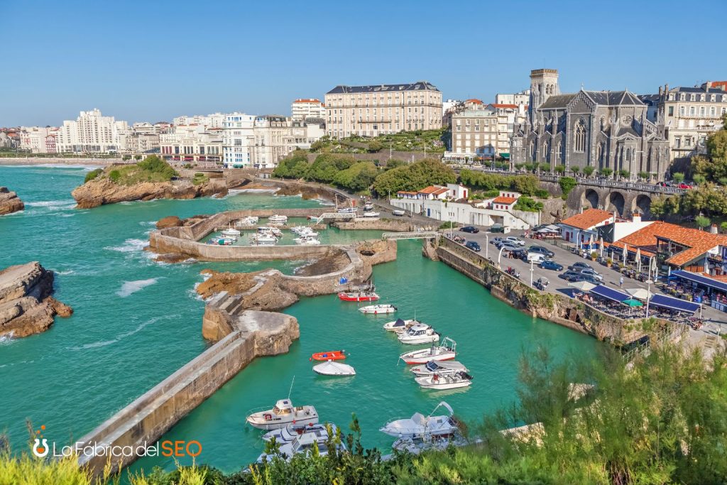 Puerto de Biarritz con barcos amarrados, aguas turquesas y la iglesia Saint-Eugénie al fondo, Francia