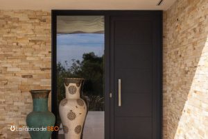 Entrada de villa de lujo con jarrón cerámico decorativo, puerta oscura moderna y pared de piedra natural