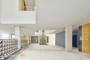Pasillo de edificio moderno con azulejos cerámicos amarillos y geométricos en blanco y negro, columnas de hormigón y patio in