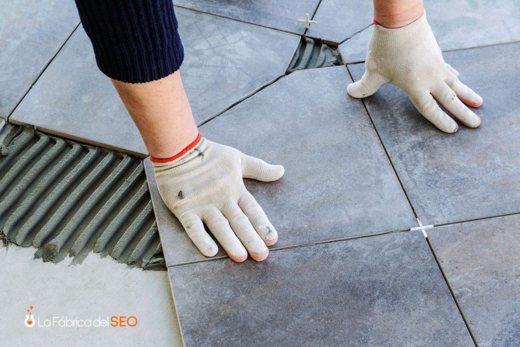 Instalación de cerámica gris en suelo con adhesivo de cemento y crucetas de nivelación por operario con guantes